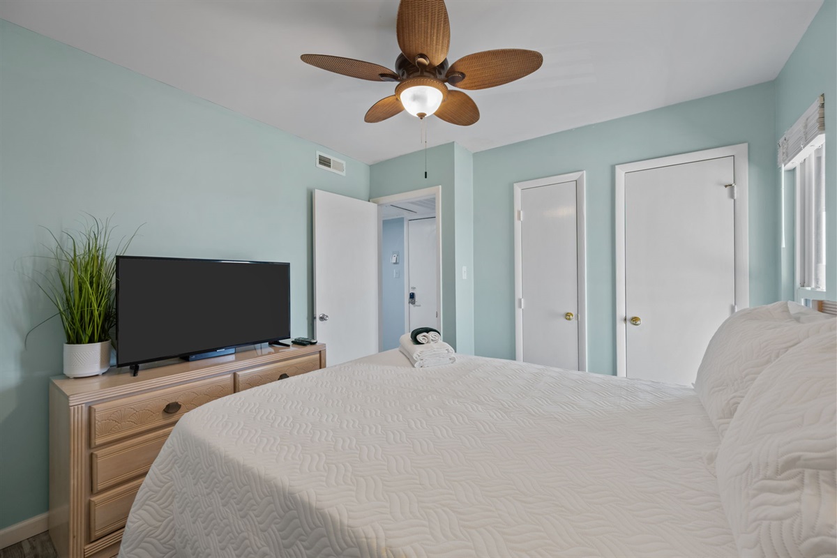 Relaxing bedroom with TV, ceiling fan, and airy coastal feel