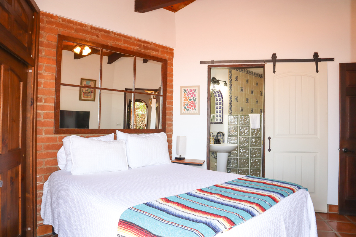 Queen-size bed, Luxury linens, Ceiling fan, French doors opening to patio, Adjacent bathroom with shower.