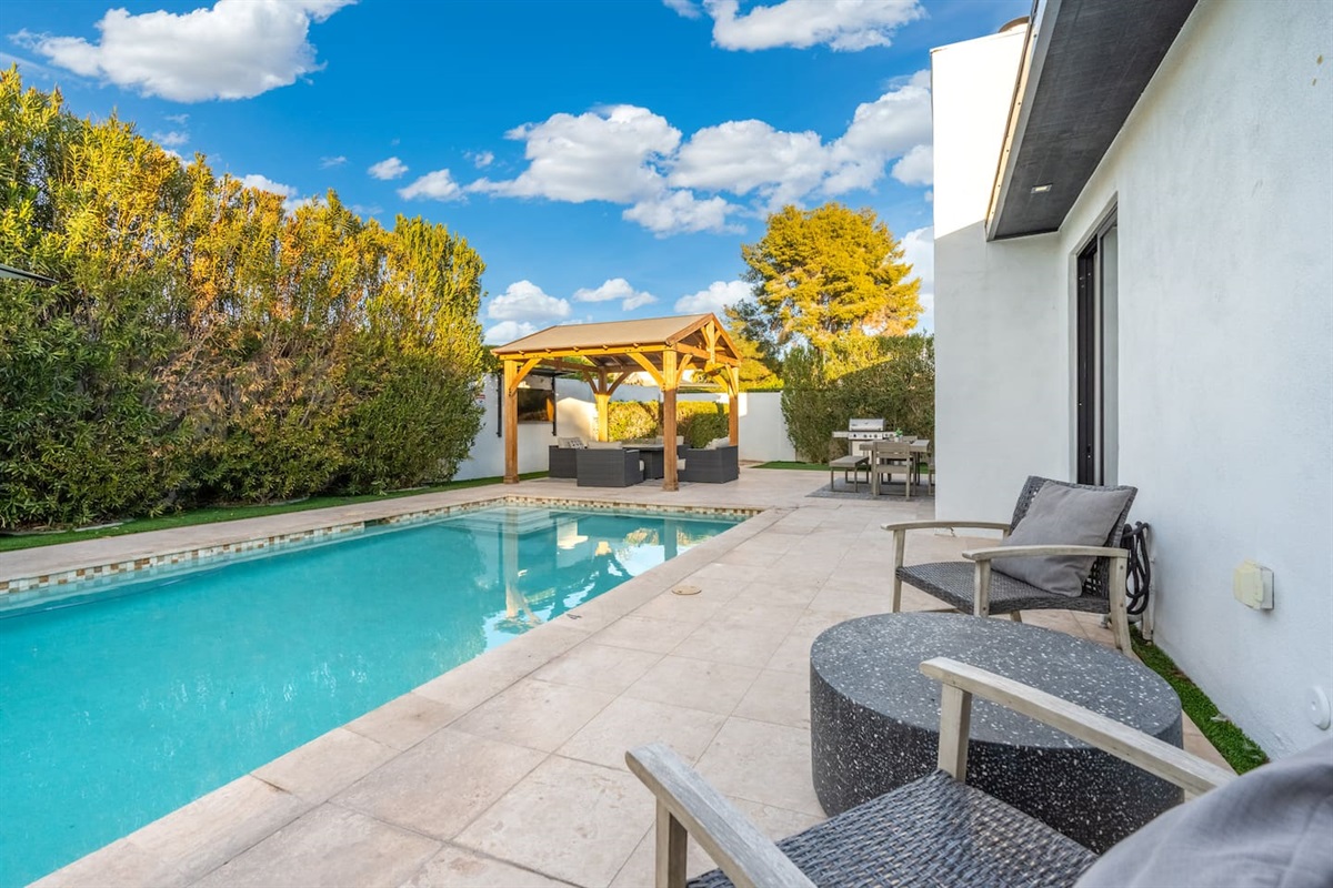 This angle captures the peaceful stretch between the lounge area and wooden pergola, with BBQ and dining close at hand.