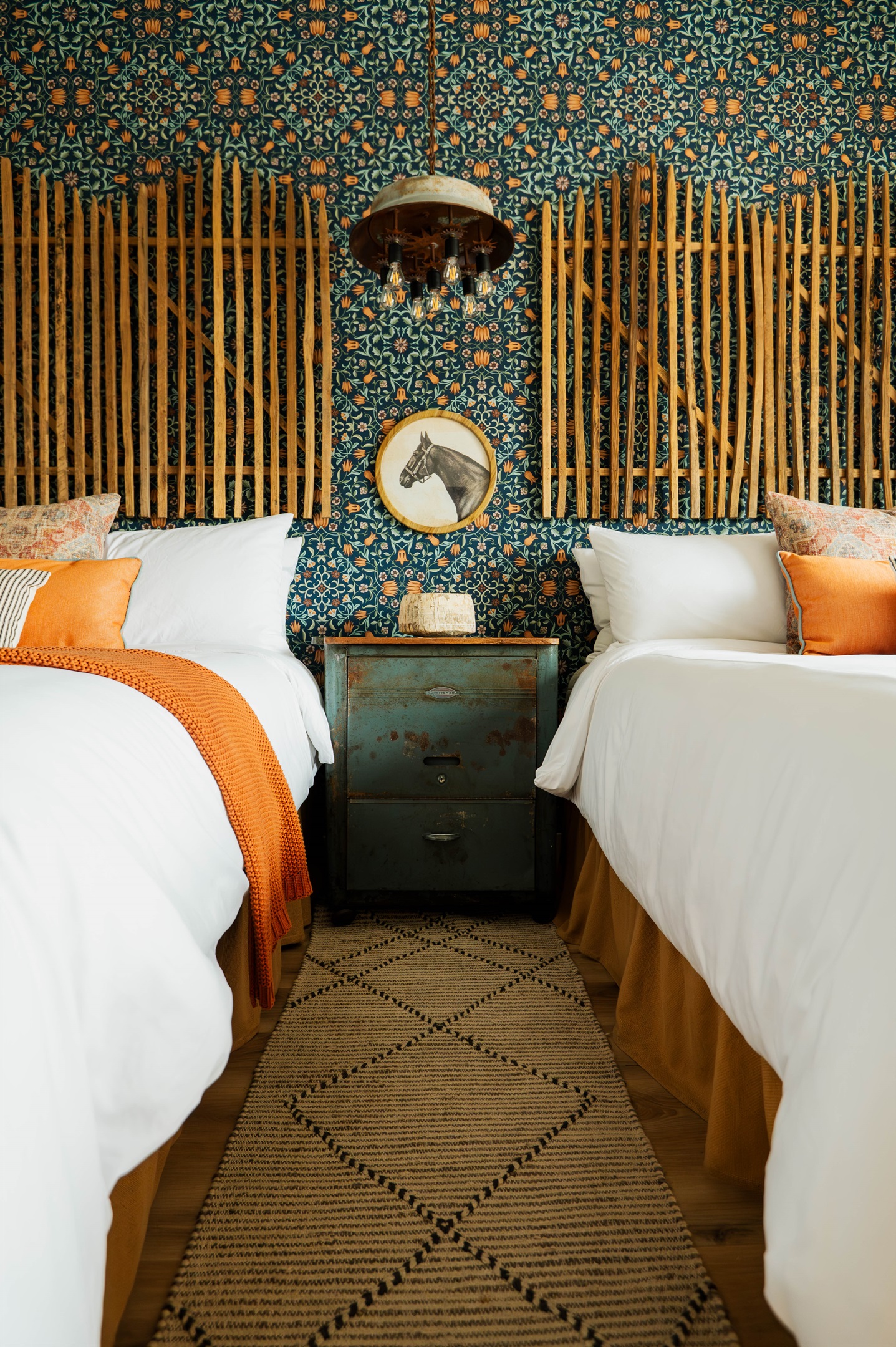 Two queen beds under a custom chandelier at the Corral Suite — designer modern Western lighting upstairs at Gaines Ranch on the Square.