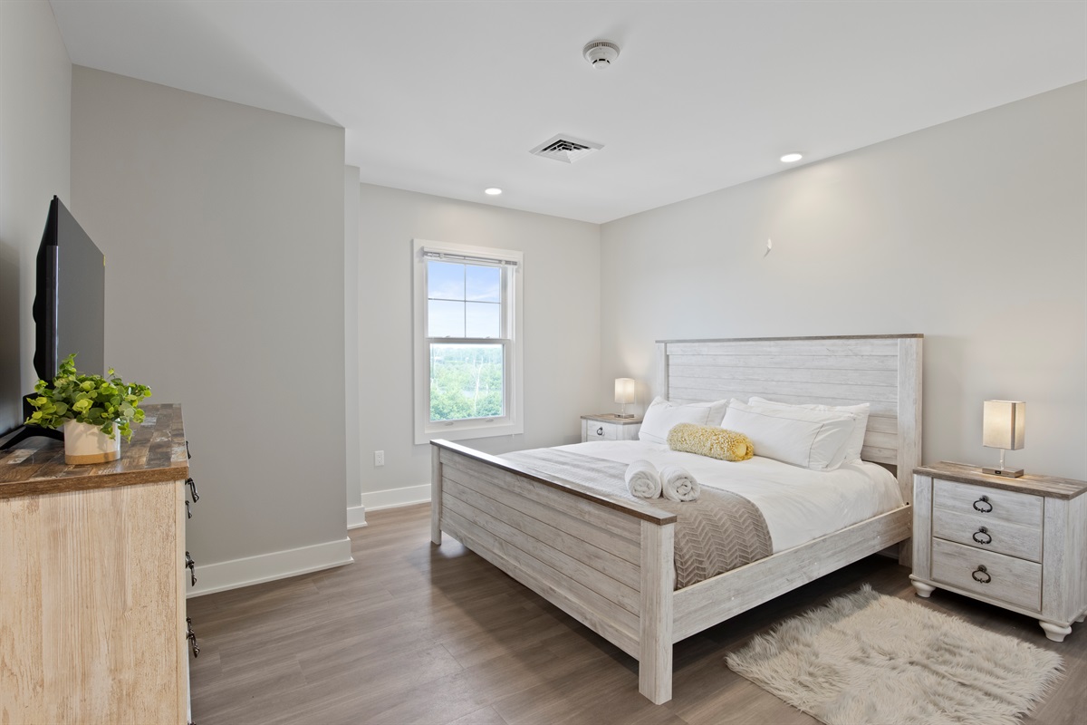 Relax in this bright and spacious bedroom featuring a cozy queen bed, modern lighting, and a serene lake-view window—perfect for your Finger Lakes getaway.