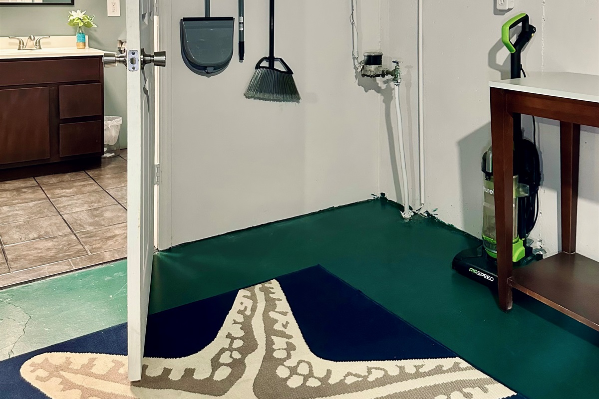 Wall-mounted cleaning station located just outside the basement bathroom. Includes a mop with extra mop pads, broom, dustpan, and vacuum, all neatly stored and easily accessible.
