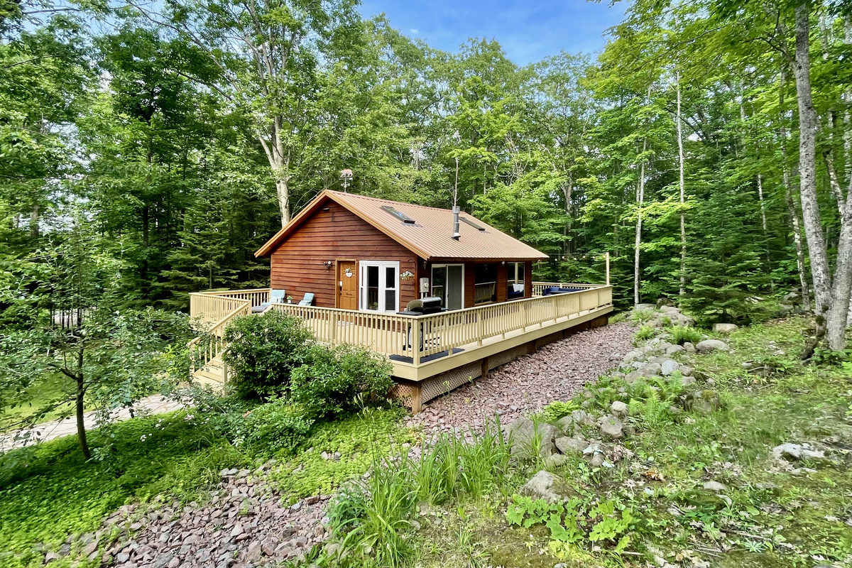 Summer view of the Main Cottage. Apple tree out front & front lounge chairs, 1k wrap around deck. Back deck dining table & lounge couch, propane fireplace (seasonal outdoor furniture May-Oct)