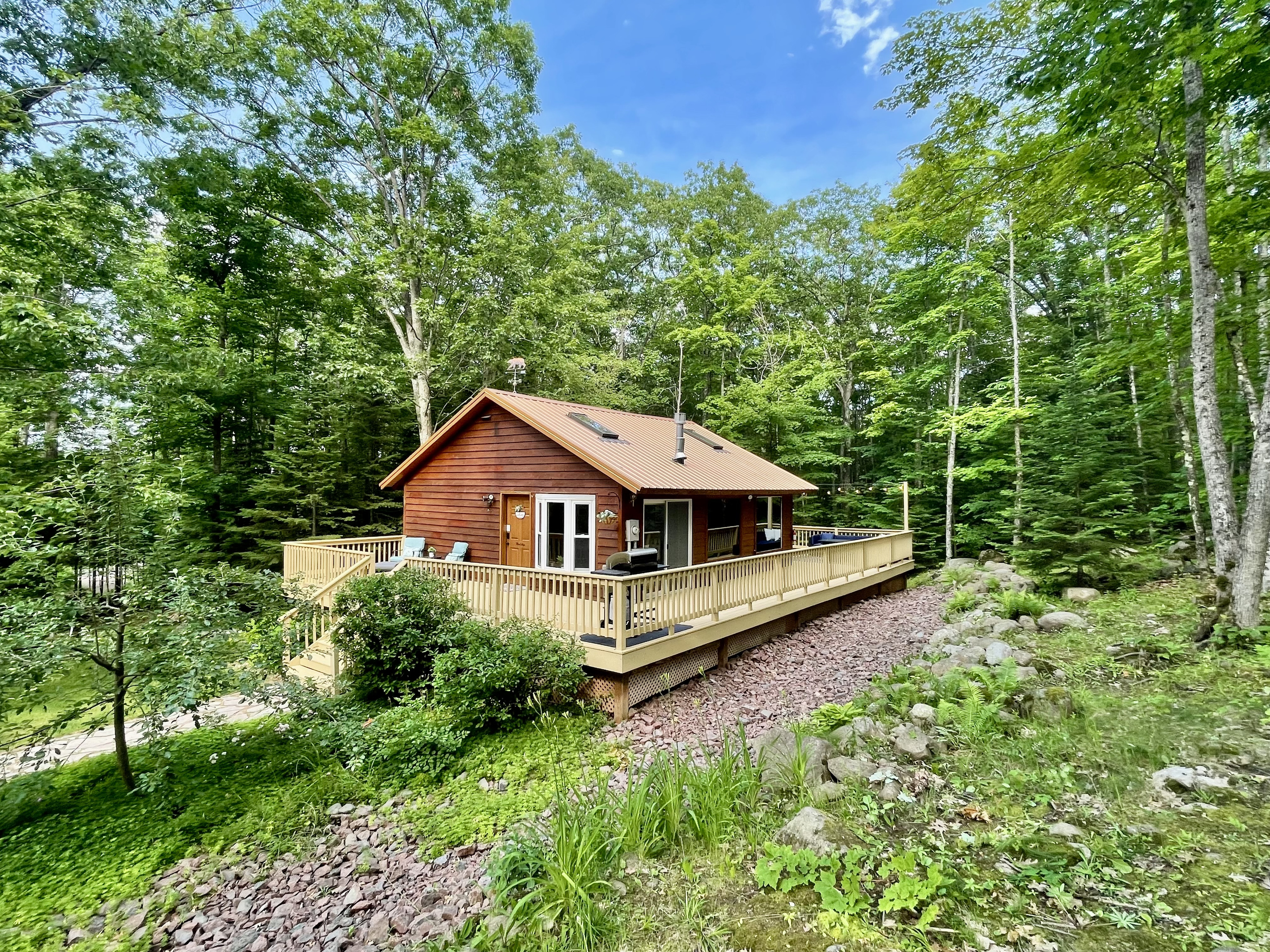 Summer view of the Main Cottage. Apple tree out front & front lounge chairs, 1k wrap around deck. Back deck dining table & lounge couch, propane fireplace (seasonal outdoor furniture May-Oct)