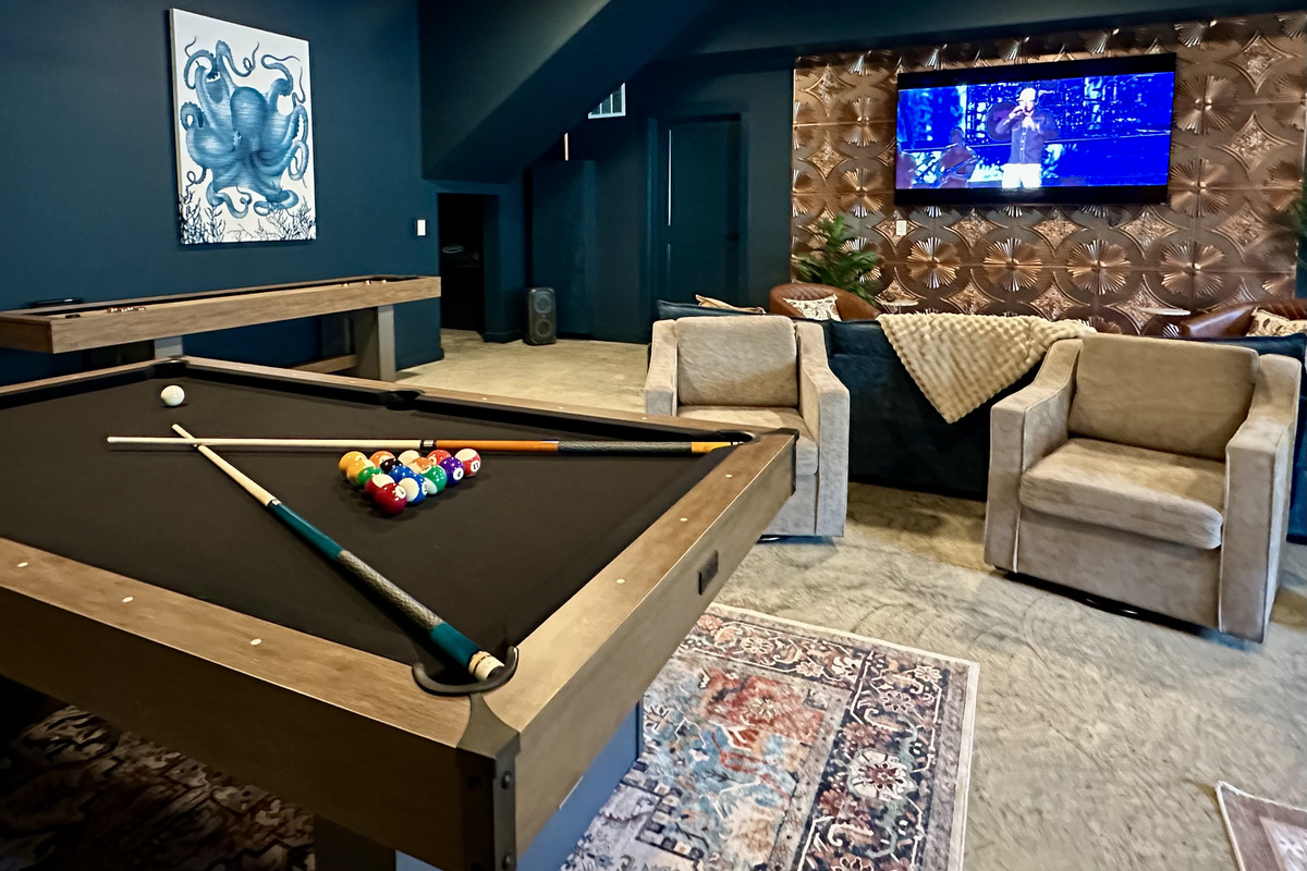 Grab a cue and break for the win under the big screen — balls racked, sports on in the background, tan lounge seating waiting for the next round.