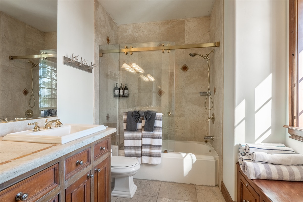 The Refined Retreat ensuite primary bathroom includes a double vanity, elegant stone finishes, and a glass-enclosed tub/shower combination.
