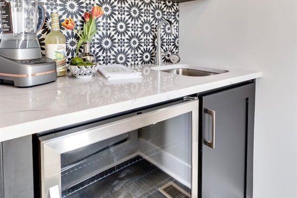 - Chic black and white backsplash adds personality to this sleek mini bar space - Includes a wine fridge, blender, and prep sink for quick drinks or smoothies - Clean countertops and fresh tulips create a polished, welcoming touch