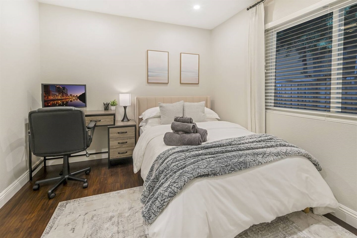 This bedroom features a desk perfect for productivity, paired with a laptop and monitor for dual-screen convenience. An ergonomic office chair ensures comfort during long work sessions, creating an ideal workspace within the cozy bedroom setting.