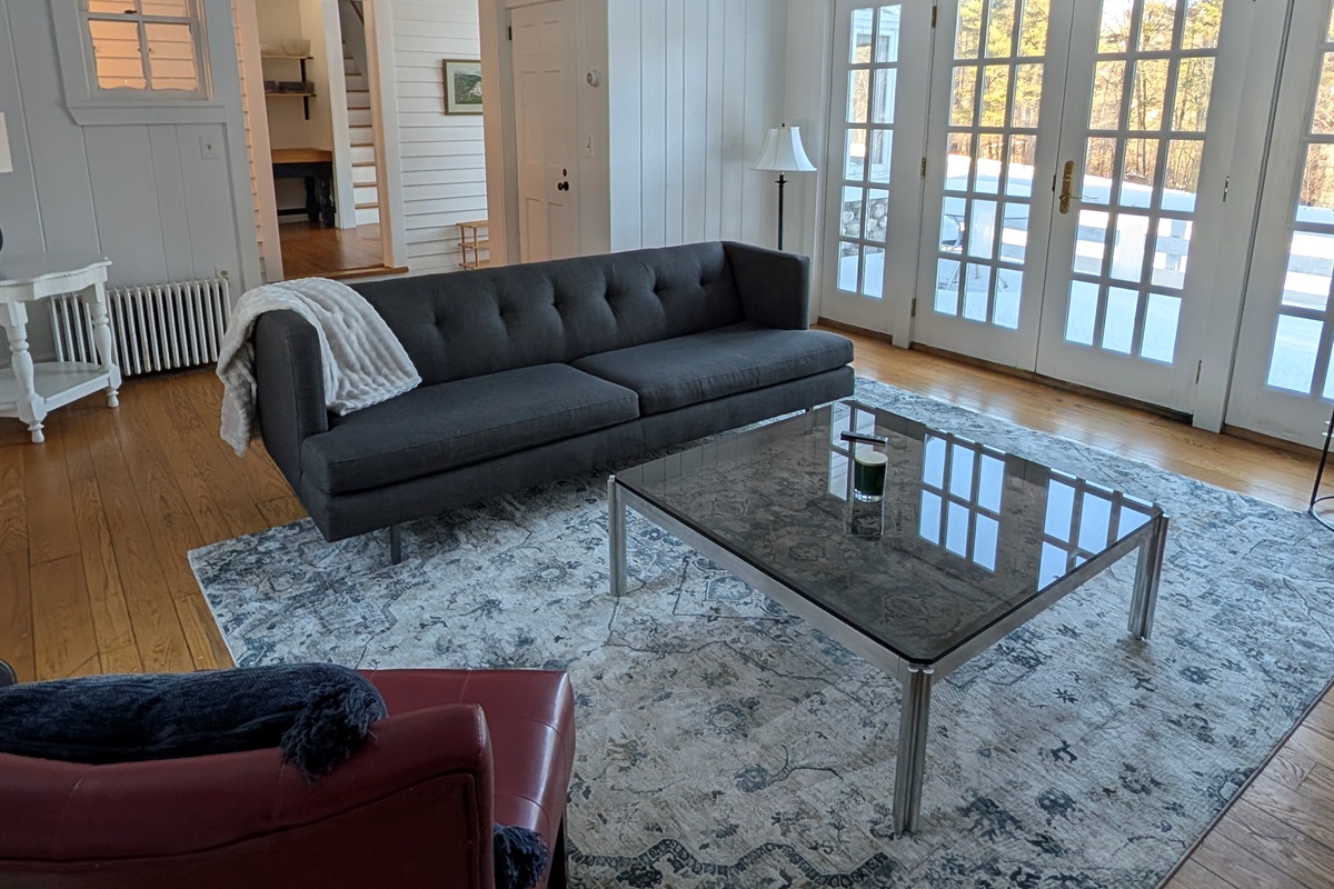 Bright and comfortable living area with modern seating, hardwood floors, and French doors opening to scenic outdoor views.