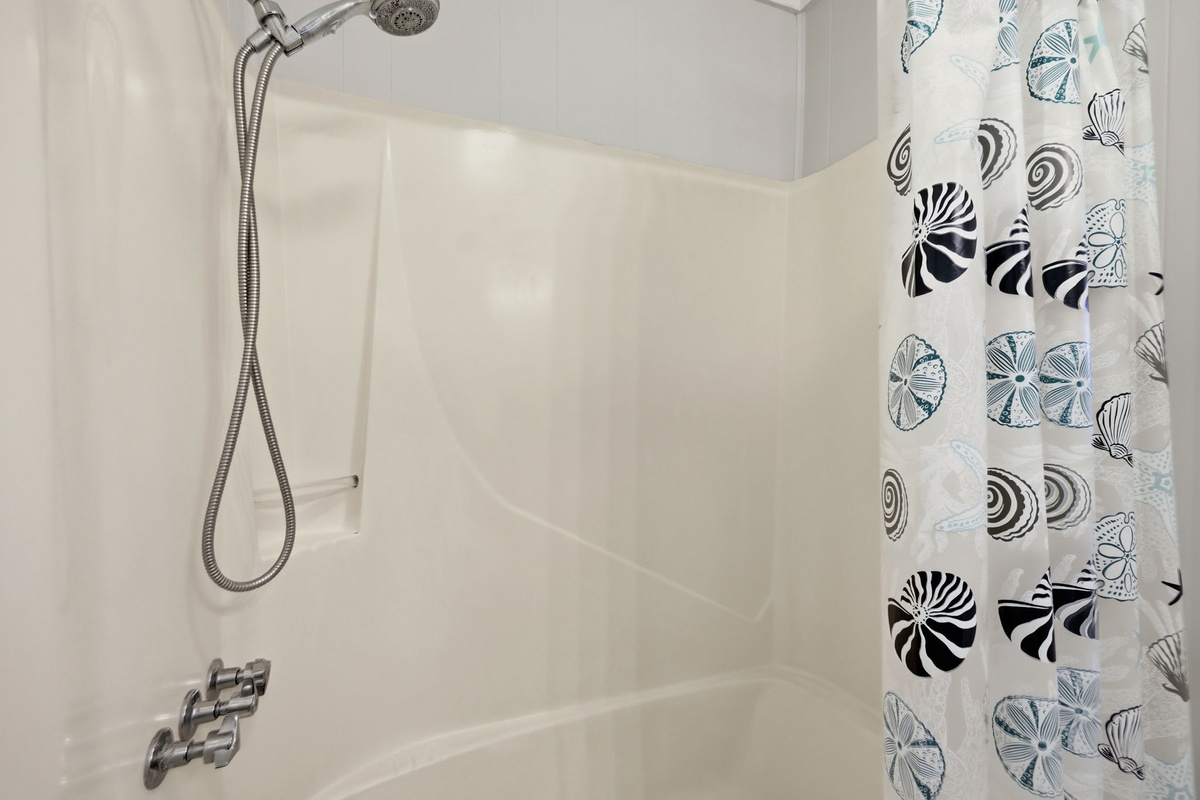Clean shower/tub combination with a handheld showerhead, perfect for relaxing after a day at the beach