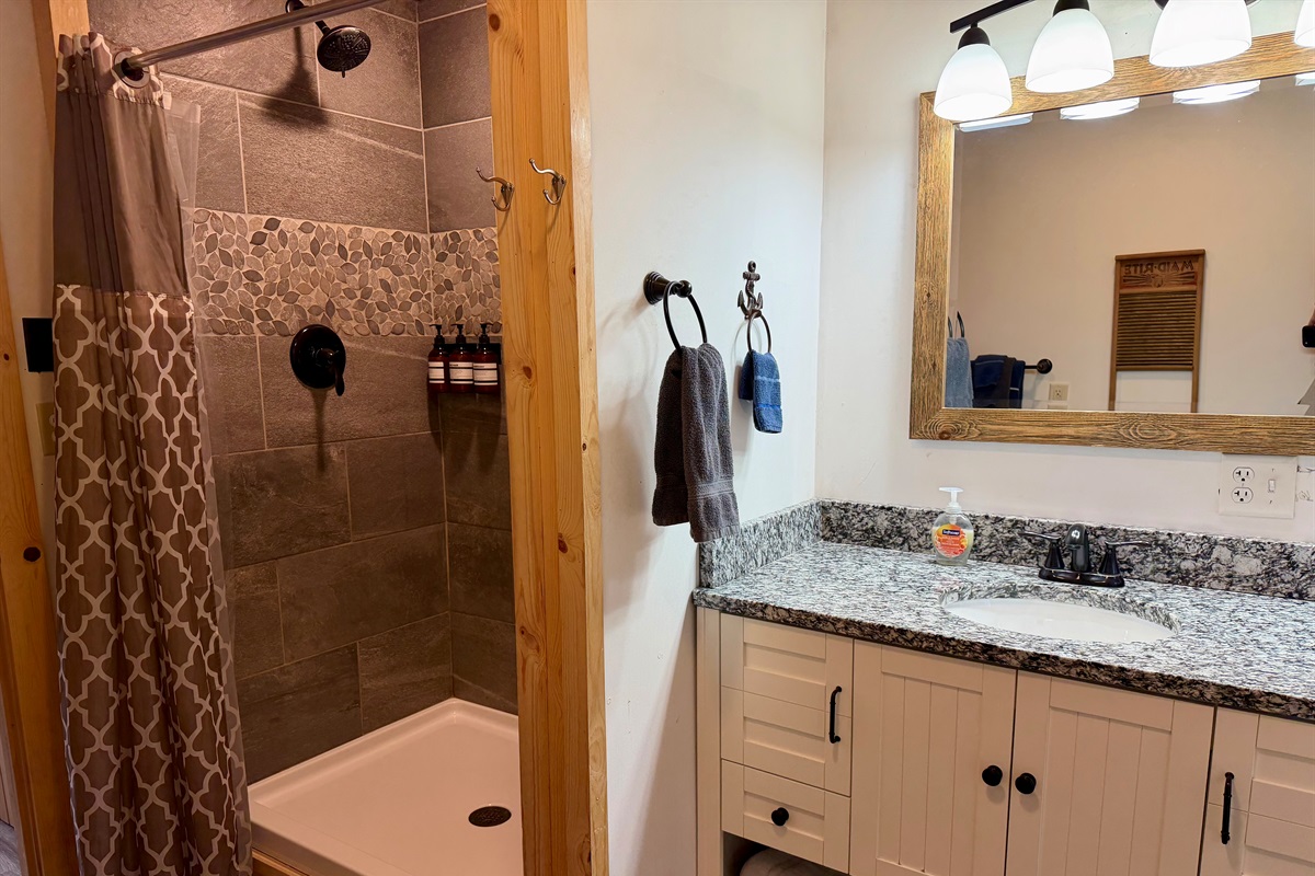 A fresh, modern shower featuring sleek stone tile and a clean, spa like feel. Stocked with wall mounted body wash, shampoo, and conditioner, it’s ready for guests to refresh and unwind in comfort.