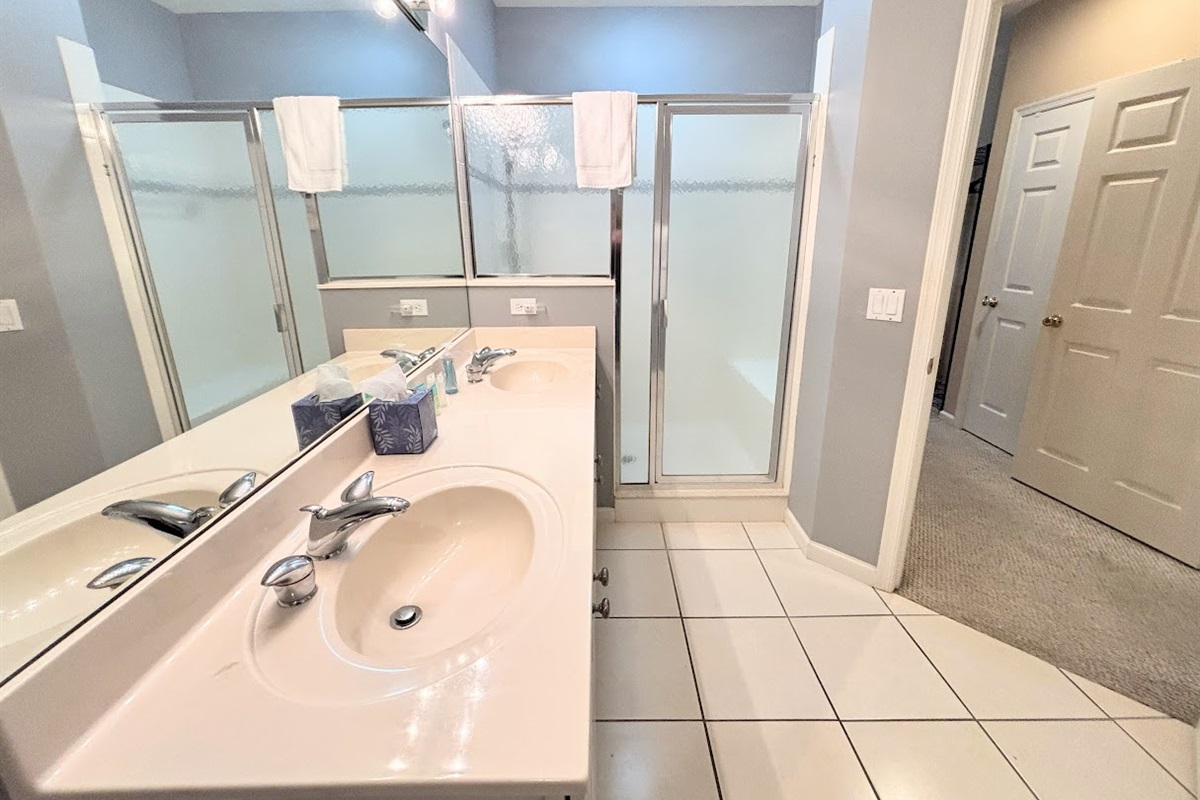 Bright bathroom with a large vanity, full mirror, tile flooring, and walk-in shower with glass doors.