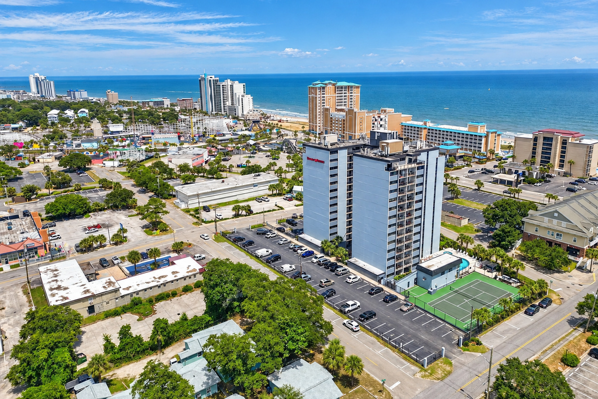 Aerial view of Holiday Towers with shared pool, hot tub, sports court, parking, and Myrtle Beach attractions nearby.