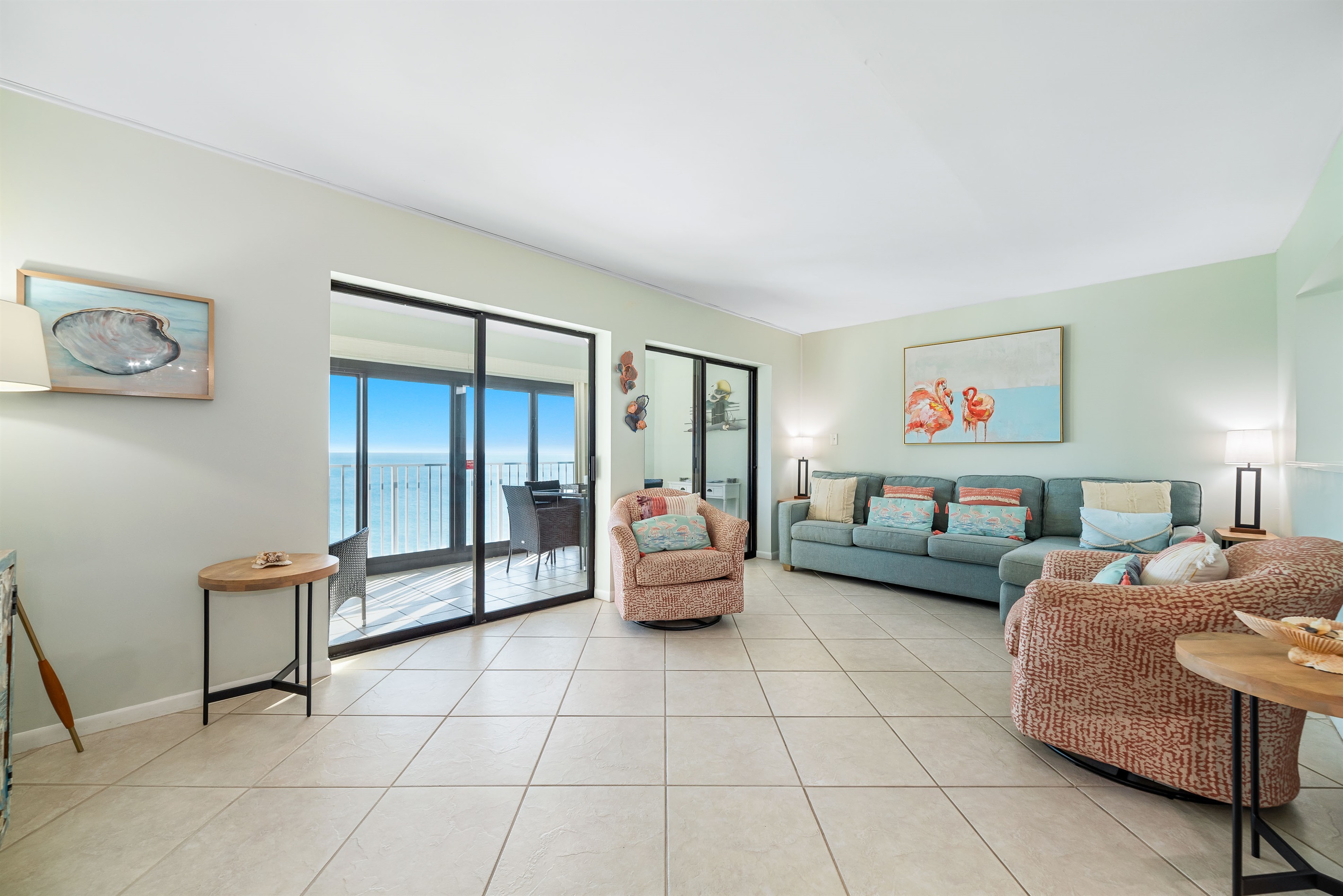 This well-appointed living room offers a comfortable sectional sofa, two swivel armchairs, and floor-to-ceiling sliding doors leading to a private balcony with panoramic ocean views.