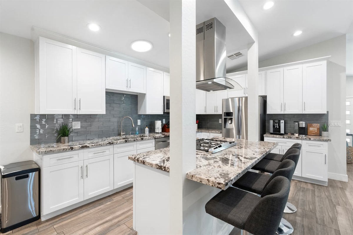 Sleek, contemporary kitchen featuring white cabinetry, granite countertops, stainless steel appliances, and a stylish bar seating area.