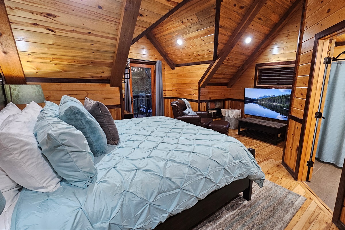 Panorama Cabin’s upstairs king bedroom includes a lounge area, a 65-inch TV, and private balcony access, providing a welcoming space to unwind after a day of exploring Broken Bow.