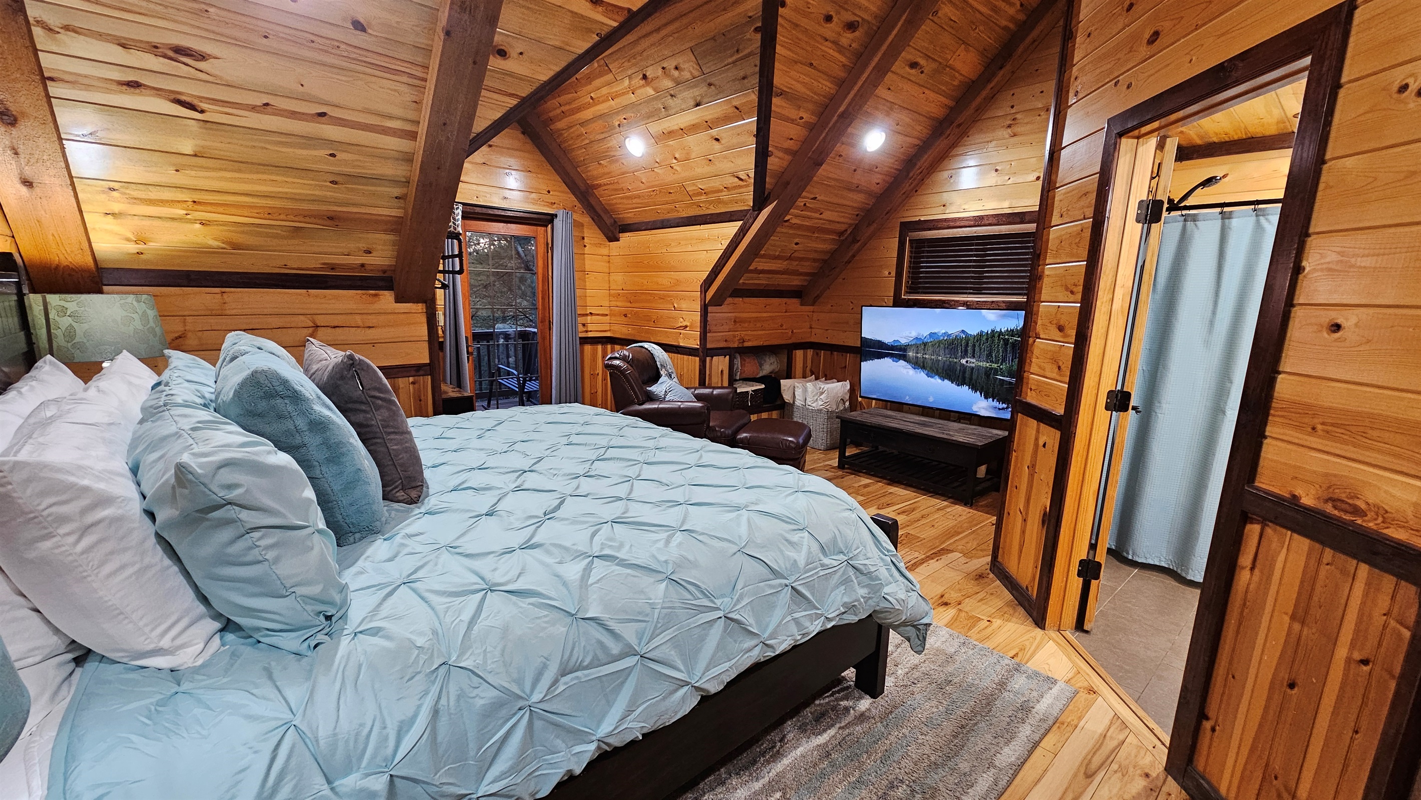 Panorama Cabin’s upstairs king bedroom includes a lounge area, a 65-inch TV, and private balcony access, providing a welcoming space to unwind after a day of exploring Broken Bow.