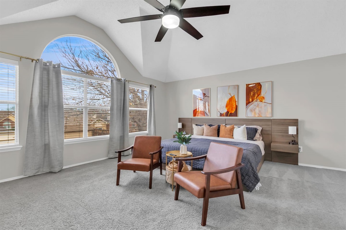 Private king bedroom with a dedicated sitting area, contemporary art, ceiling fan, and blackout shades designed for comfort and relaxation.