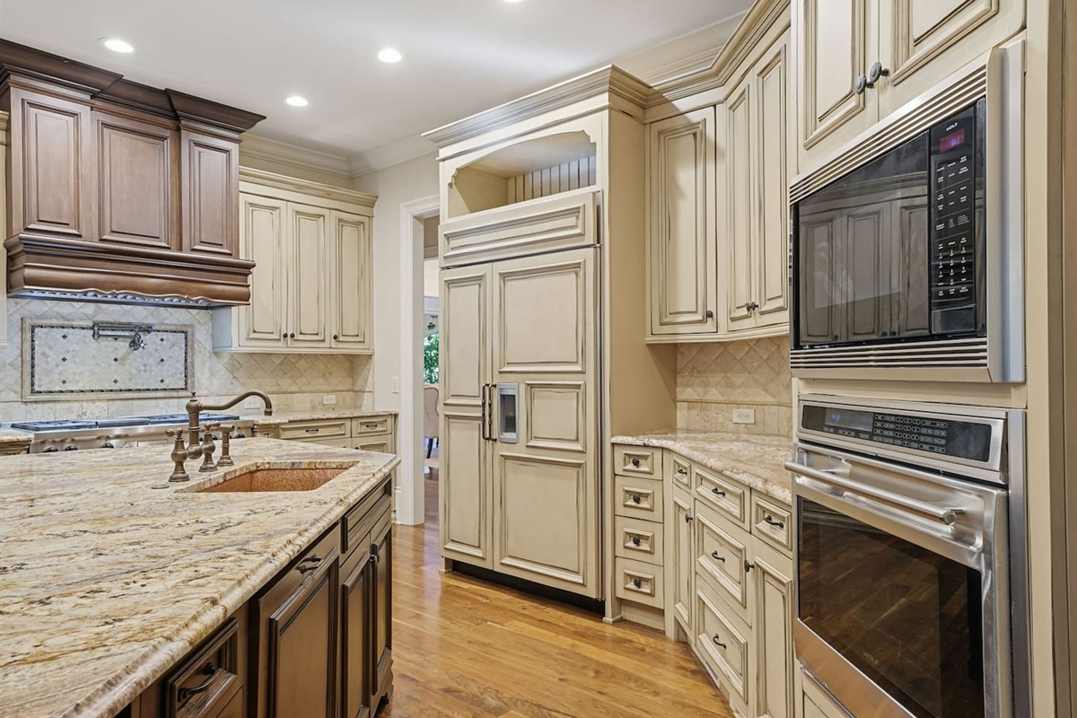 This open kitchen features beautiful cream wood cabinetry, sleek granite countertops, and an island that comfortably seats four. The bright, airy design makes it the perfect place to cook, gather, and share meals together.