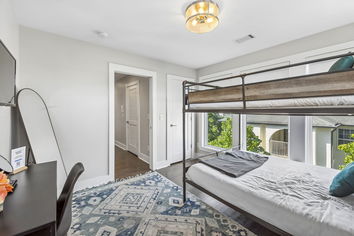Queen over Queen bunk framed by oversized windows & natural light - Soft layered bedding with patterned pillows create a cozy and inviting sleep space - Easy access to hallway & shared areas makes this room perfect for families or groups