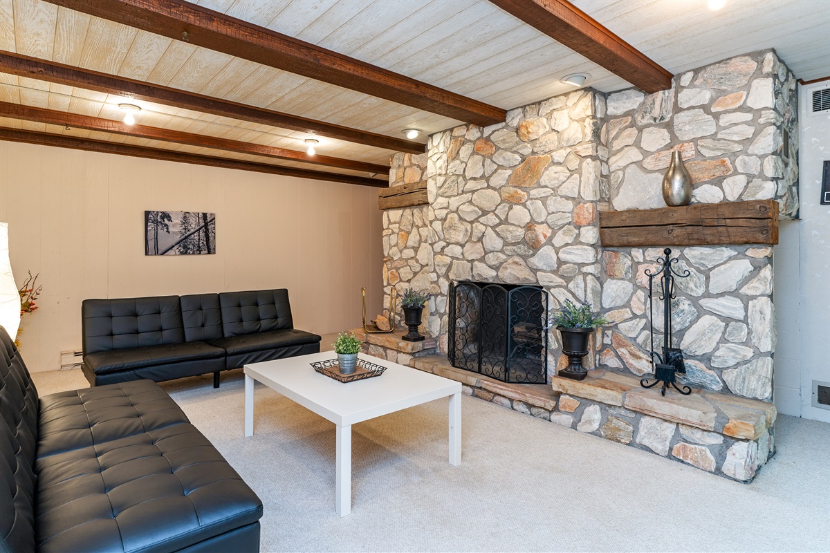 Unwind in the inviting basement level living room with plush seating and a stunning stone fireplace – a perfect spot for cozy evenings.