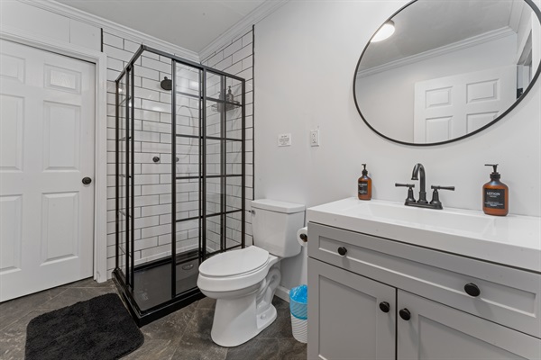 Modern, spotless bathroom featuring a stylish black-framed walk-in shower, spacious vanity, and all essentials provided for a comfortable stay.