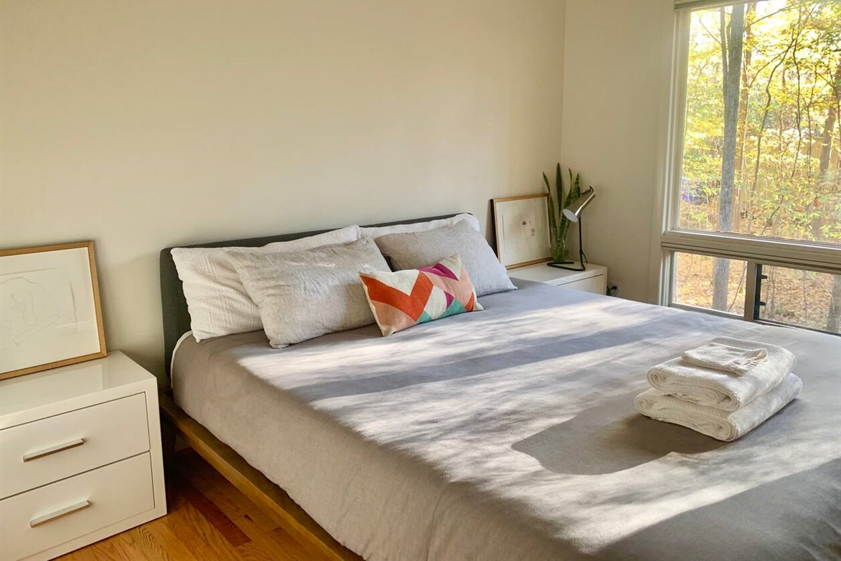 Another light-filled bedroom framed by picture windows and treetops &mdash; roomy, quiet, and made for sleeping in.