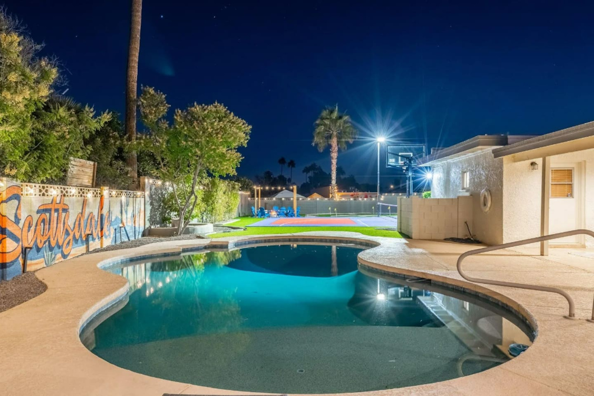 The pool glows at night, with the sport court lit just beyond — pick your pace, the whole backyard is yours.