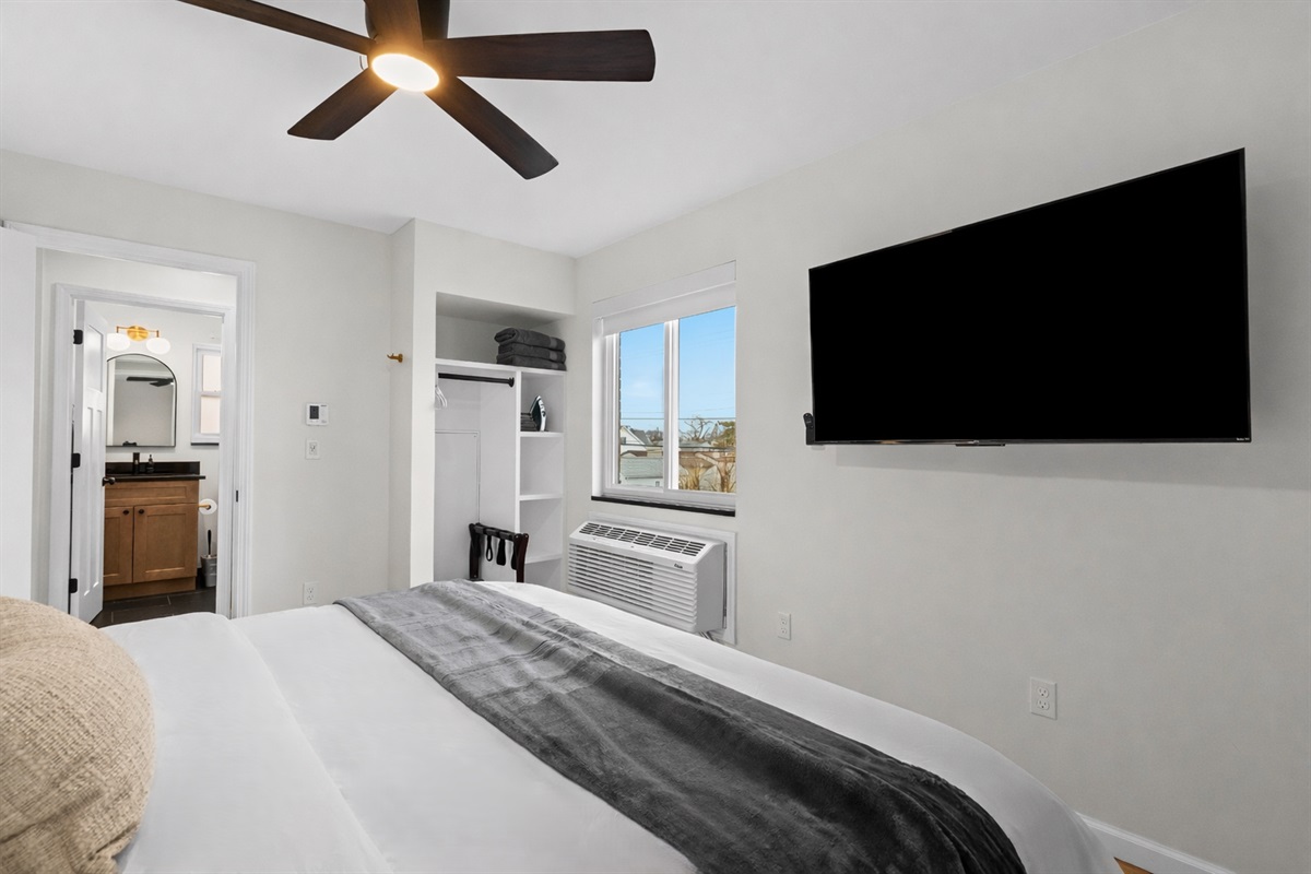 Relaxing bedroom retreat with plush bedding, ceiling fan, smart TV, and bright window—designed for comfort, convenience, and restful nights.