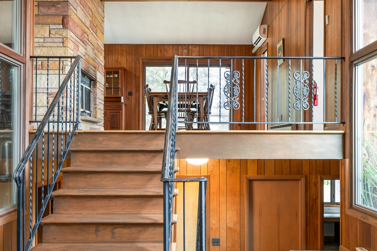 Step into warmth with soaring windows, wood-paneled walls, and a charming stone fireplace that welcomes you into this inviting retreat.