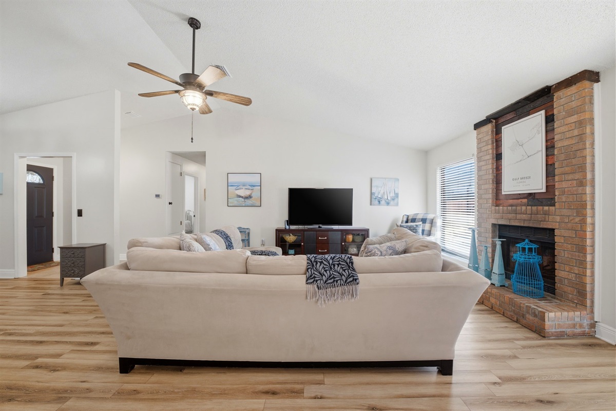 The living room is designed for comfort and connection, with plush seating, a large TV for movie nights, and a classic brick fireplace as a centerpiece. The open floor plan and vaulted ceilings provide a bright, relaxing space to enjoy during your stay.