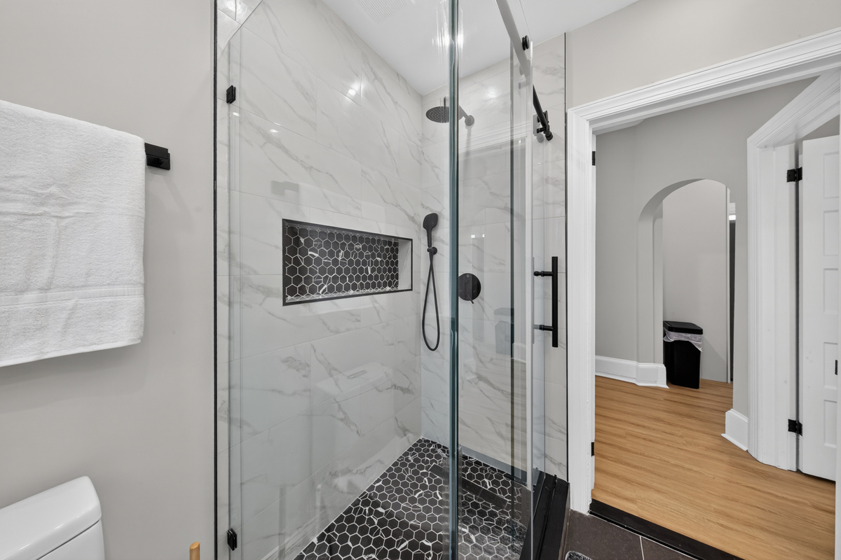 Spa-inspired walk-in shower with frameless sliding glass door, natural river stone floor, and rain showerhead.