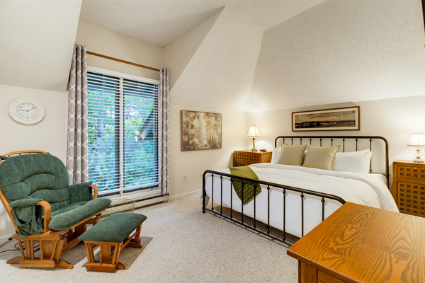 The inviting second bedroom features a king bed, a comfortable reading chair, and wooded views.