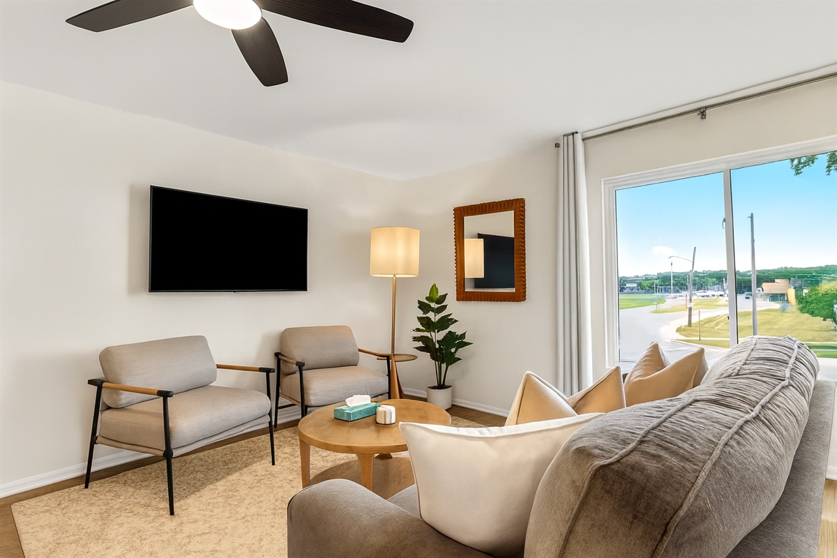Bright living area with mounted Smart TV, cozy armchairs, and vibrant artwork to welcome you in.