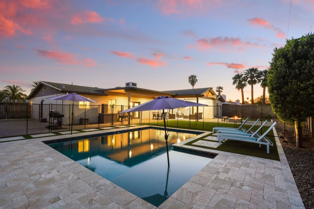 Private backyard pool with lounge chairs, umbrella shade, fire pit seating, and a bright outdoor space 