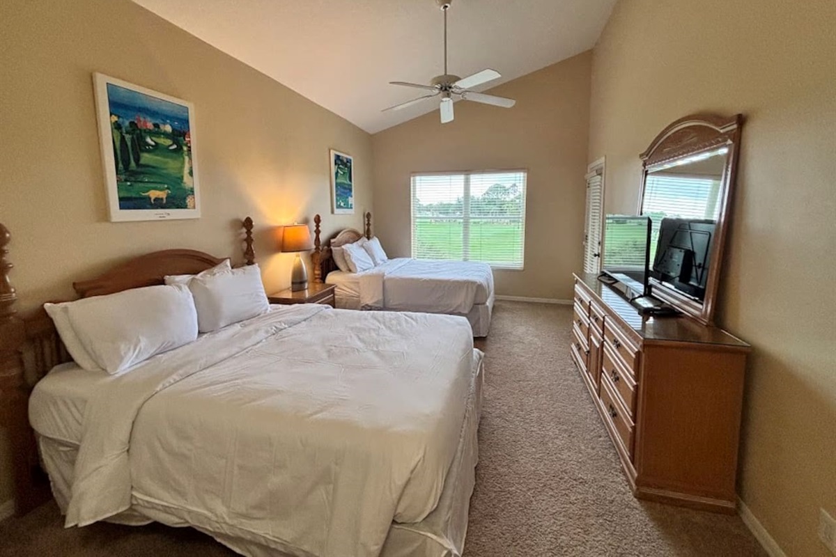 Spacious bedroom featuring two beds, ceiling fan, dresser storage, TV, and natural light.