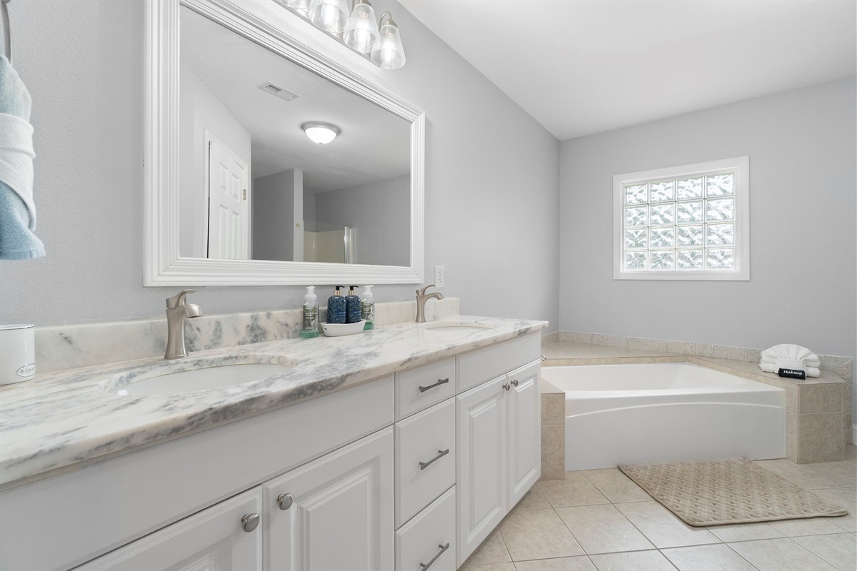 This spacious bathroom boasts dual sinks for convenience, a deep soaking tub for relaxation, and clean, sophisticated design throughout. The subtle coastal tones pair perfectly with the airy layout, offering both style and comfort.