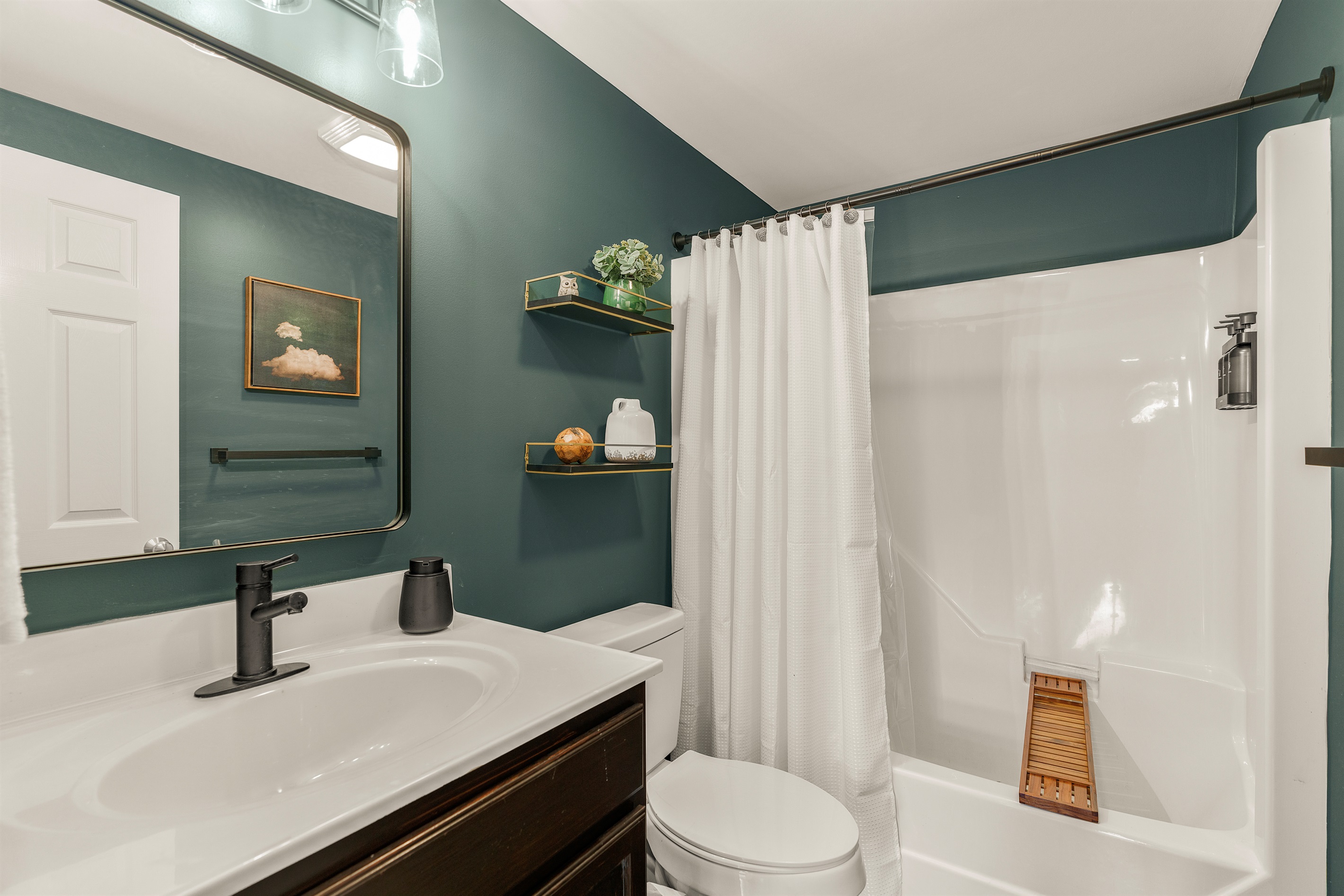 Sophisticated and spirited. This hall bath features fresh black fixtures, a jade-meets-forest green wall tone, curated decor, and full shower/tub combo—shared but never short on style