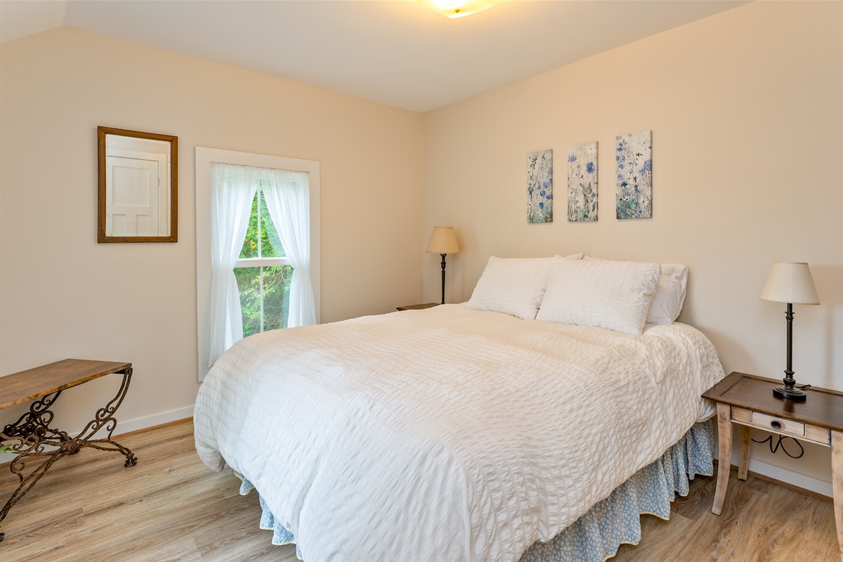 Inviting bedroom with serene views, soft natural light, and a plush white comforter for restful nights. Bedroom #1 Queen