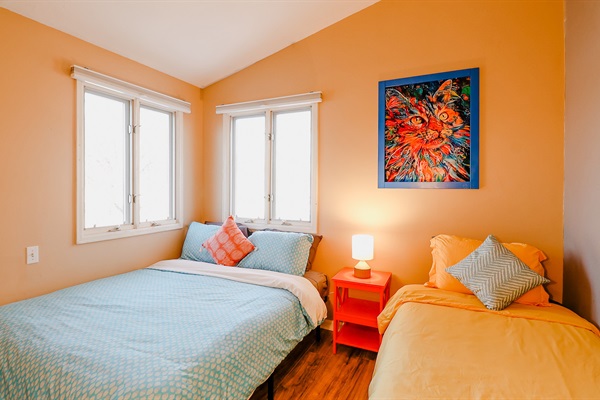 A bedroom with a dynamic color scheme, featuring a blue bedsheet on one bed and an orange bedsheet on another, against a backdrop of an orange wall, creating a lively and energetic atmosphere.