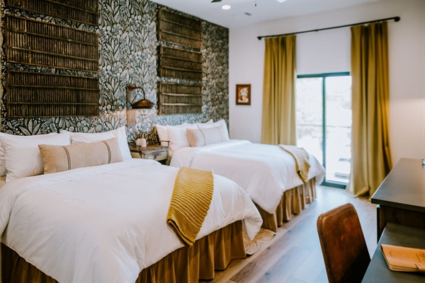 Inside the Lazy Spur Suite &mdash; two queen beds, natural light through curated drapery, and modern Western design upstairs at Gaines Ranch on the Square.