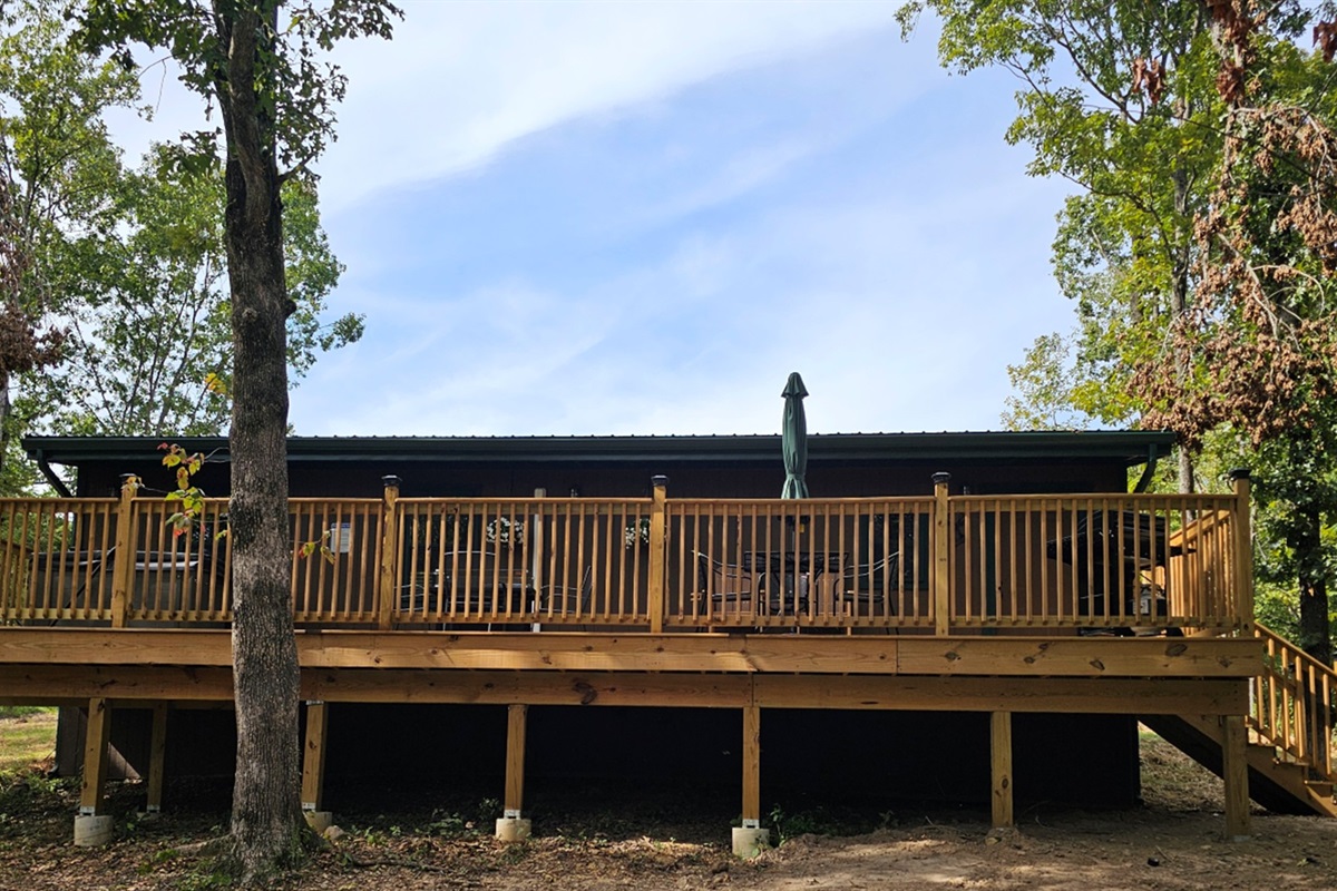 Back view of the cabin with a large wooden deck, outdoor seating, and forest setting