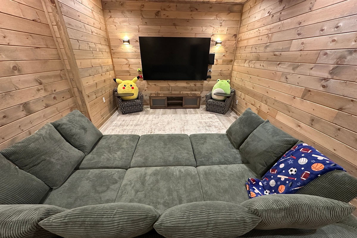 A cozy movie nook made for downtime and laughs. Plush seating, warm wood walls, and a big screen create the perfect spot for kids to unwind or for relaxed movie nights after a full day outdoors.