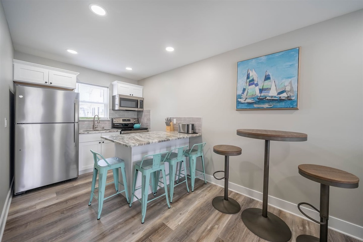 Bright, modern kitchen with stainless steel appliances, stone countertops, and a spacious island with bar seating. Designed for easy meals and casual gatherings, the open layout makes cooking and dining feel relaxed and social.