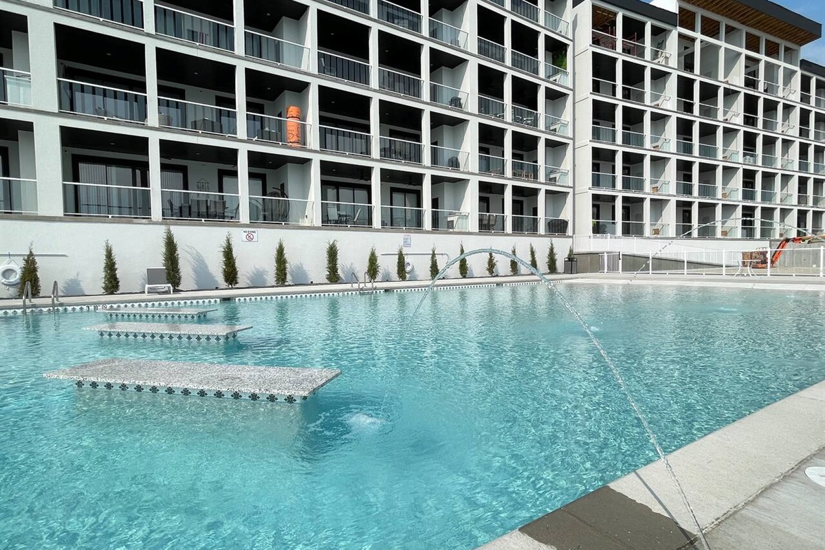 One of two pools for guests. Tables in the deep end with beach entry design in the shallow end, with spraying fountains. 