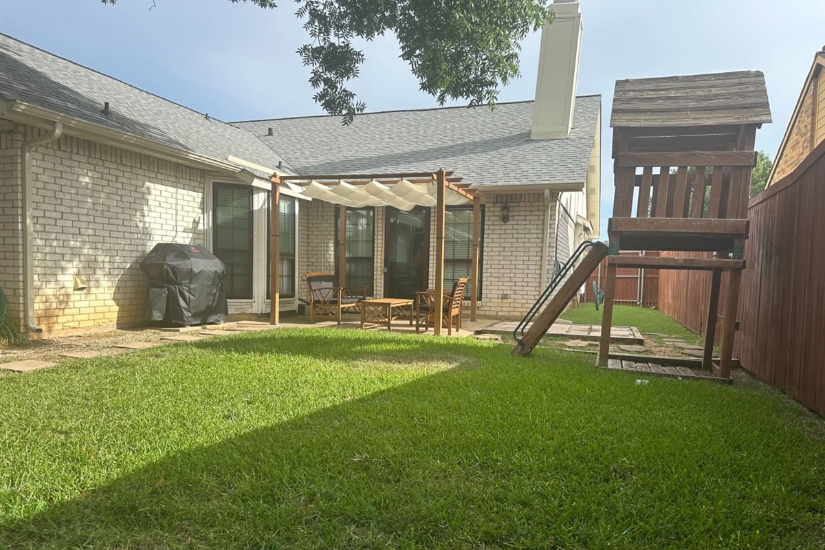 Private backyard with shaded seating and playset — ideal for family fun.