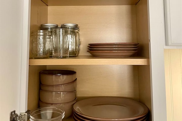 Well-stocked kitchen cabinet with a complete set of dishware, glasses, mugs, and bowls for everyday meals.