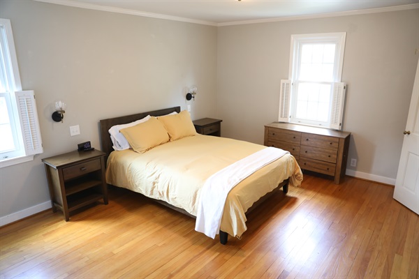 NW Bedroom showing queen size bed, nightstands with alarm clock, wall mounted lamps, dresser, and Roku TV