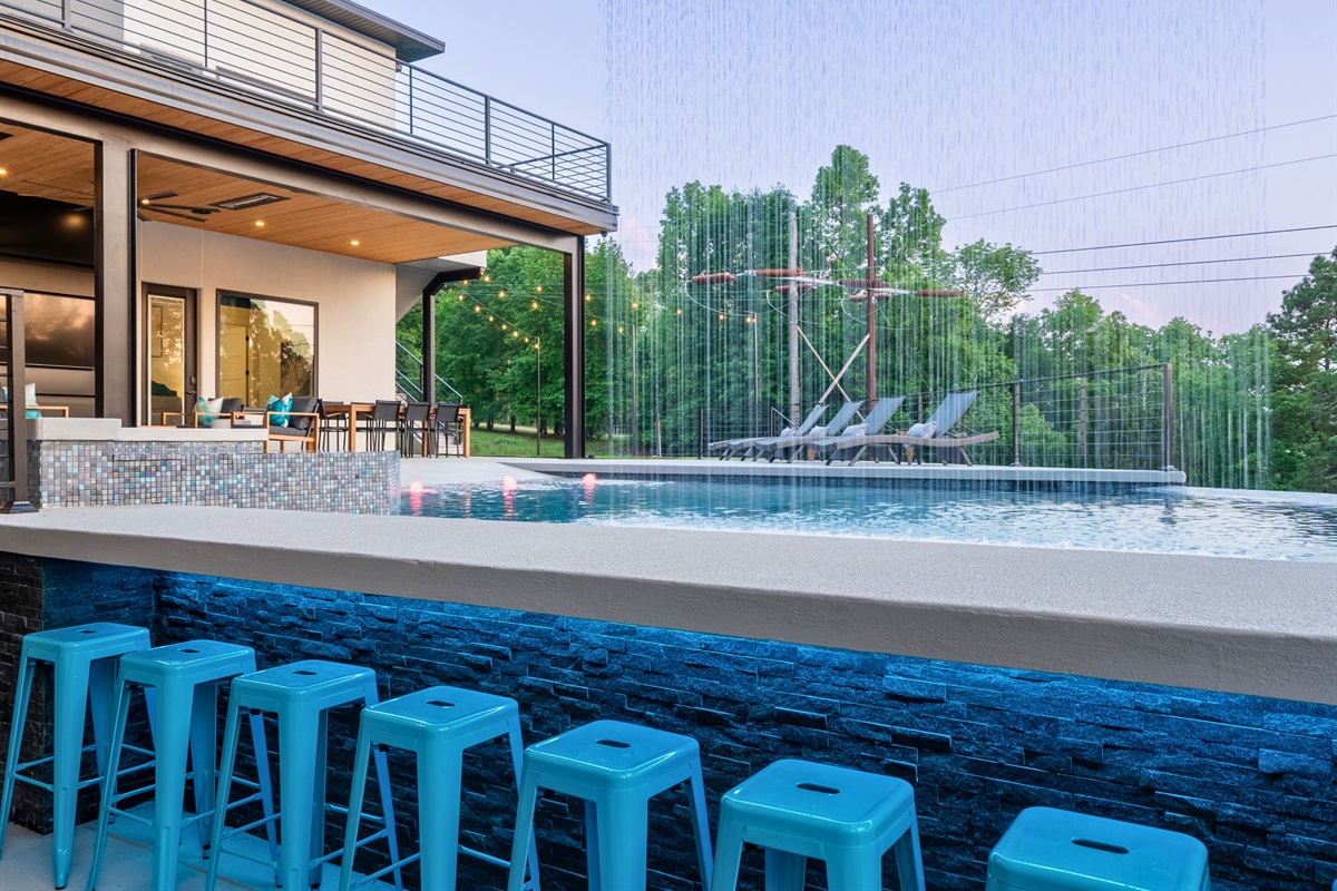 The poolside bar, with its vibrant blue stools and cascading waterfall, offers a perfect spot for enjoying drinks and conversation.