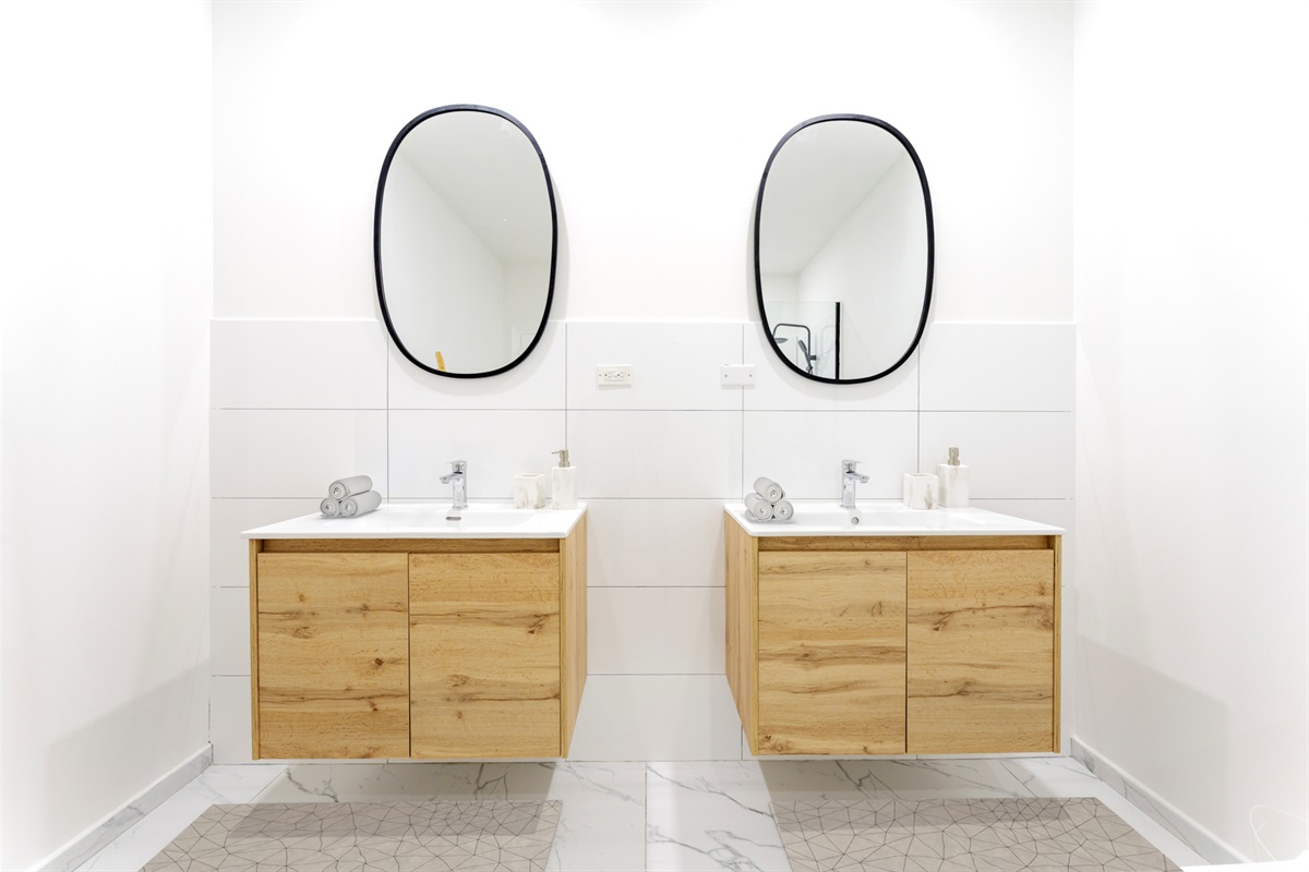 Dual vanities with oval mirrors and natural wood cabinetry in the primary bathroom